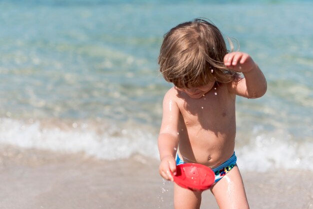 Bambino sorridente del colpo medio che gioca con acqua alla spiaggia