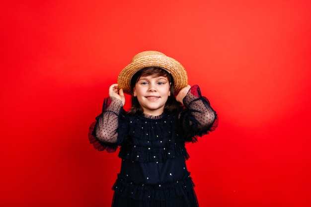 bambino sorridente in cappello di paglia. Bambina di risata che posa in vestito nero.