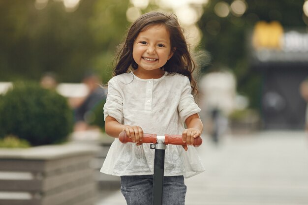 Bambino sul motorino di scossa nel parco. I bambini imparano a pattinare sul roller. Bambina che pattina sulla soleggiata giornata estiva.