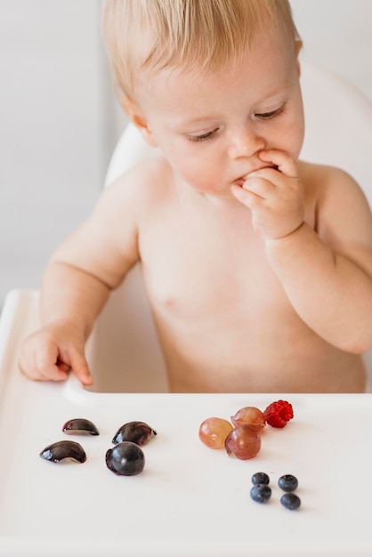 Bambino sveglio nel seggiolone scegliendo quale frutta mangiare