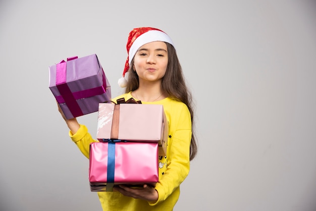 Bambino vestito con cappello rosso di Babbo Natale che trasporta molti regali di Natale. Foto di alta qualità