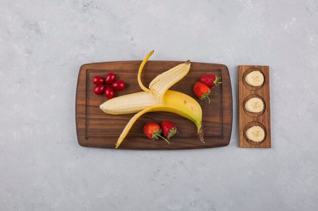 Banana, fragola e frutti di bosco su un piatto di legno al centro