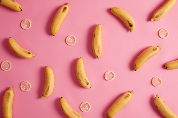 Banane e contraccettivi su sfondo rosa. Preservativo al gusto tropicale per una relazione sicura. Eliminazione del rischio di gravidanza. Fornitore di servizi sanitari. Preservativo testato per resistenza, flessibilità, affidabilità