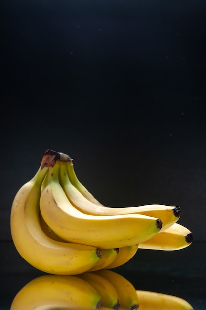 Banane gialle fresche di vista frontale su un'oscurità di colore esotico tropicale della frutta nera della parete