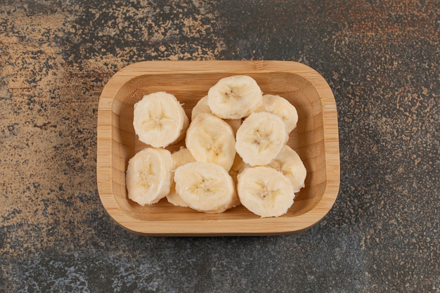 Banane sbucciate a fette sul piatto di legno.