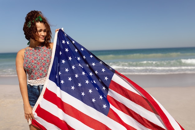 Bandiera americana della tenuta della bella donna sulla spiaggia nella sunshifcane