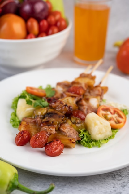 Barbecue con una varietà di carni, completo di pomodori e peperoni su un piatto bianco.