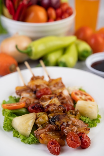 Barbecue con una varietà di carni, completo di pomodori e peperoni su un piatto bianco.