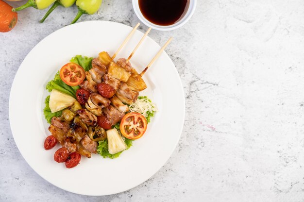 Barbecue con una varietà di carni, completo di pomodori e peperoni su un piatto bianco.