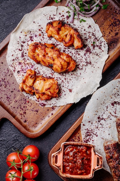 Barbecue di pollo servito con sumakh ed erbe su pane lavash.