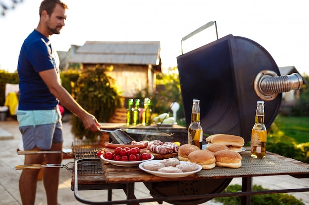 Barbecue di torrefazione del giovane sulla griglia nella campagna del cottage.