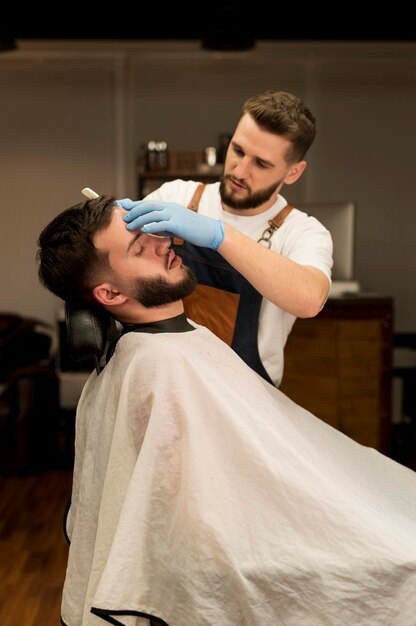 Barbiere che rade e modella la barba del cliente maschio male