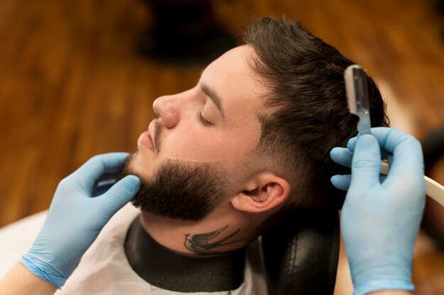 Barbiere che rade e modella la barba del cliente maschio male