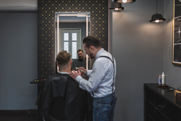 Barbiere che rade i capelli del cliente vicino allo specchio
