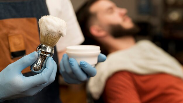 Barbiere che usa la crema da barba per contornare la barba del cliente maschio