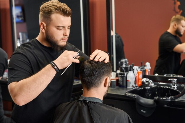 Barbiere competente che taglia i capelli del cliente con forbici affilate