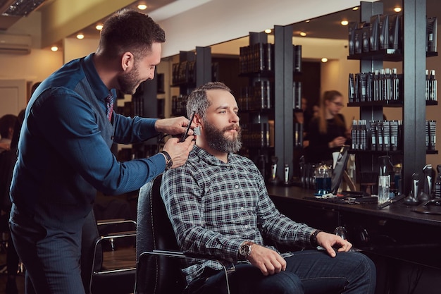 Barbiere professionista che lavora con un cliente in un salone di parrucchiere. Acconciare la barba con un rifinitore.