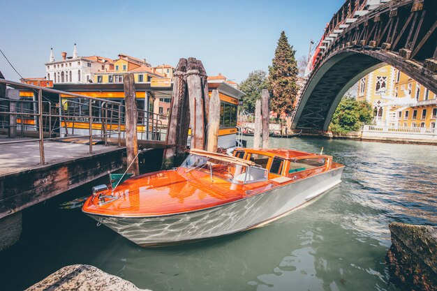 Barca arancio del canale navigabile su un fiume sotto un ponte vicino alle costruzioni a Venezia, Italia