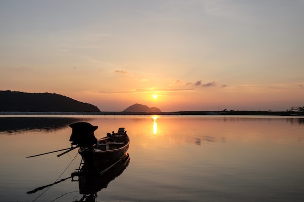 Barca sul mare circondata da colline con il sole che si riflette sull'acqua durante il tramonto