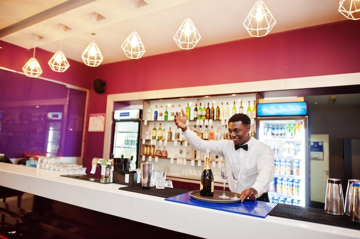 Foto gratuito barista afroamericano al bar che tiene champagne con bicchieri sul vassoio