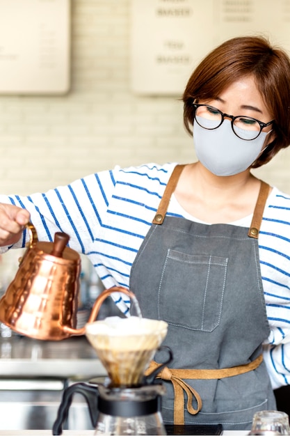 Barista coreano in maschera per il viso versando il caffè a goccia al caffè