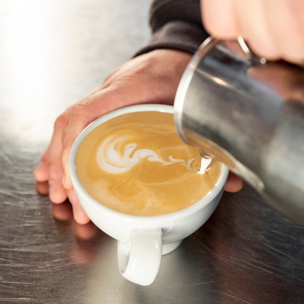 Barista del primo piano che versa caffè caldo nella tazza