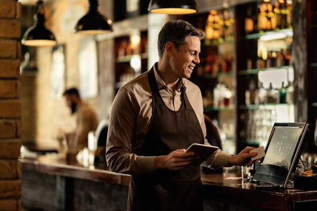 Barista felice che aggiunge un ordine al registratore di cassa mentre lavora in un pub