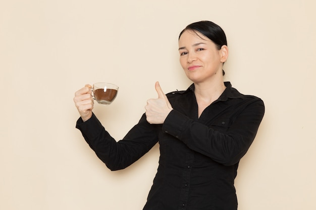 barista femmina in pantaloni camicia nera che tiene tazza di caffè sul muro bianco