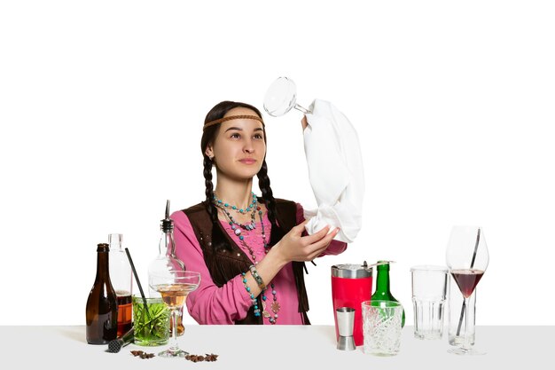 Barista femminile esperto sta preparando cocktail in studio isolato sul muro bianco