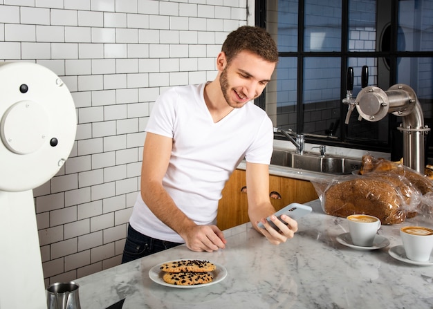 Barista in piedi con lo smartphone dietro il bancone