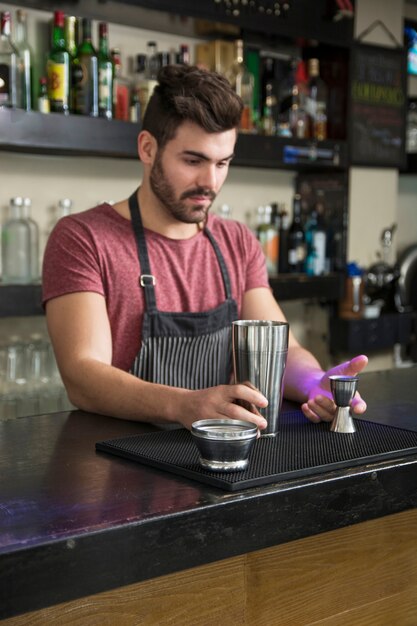 Barista maschio aggiungendo ingrediente in shaker al bancone del bar