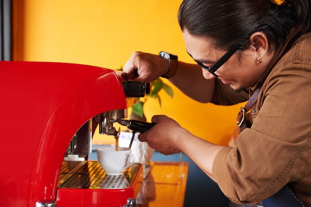 Barista maschio asiatico che produce tazza di caffè sulla macchina del caffè espresso