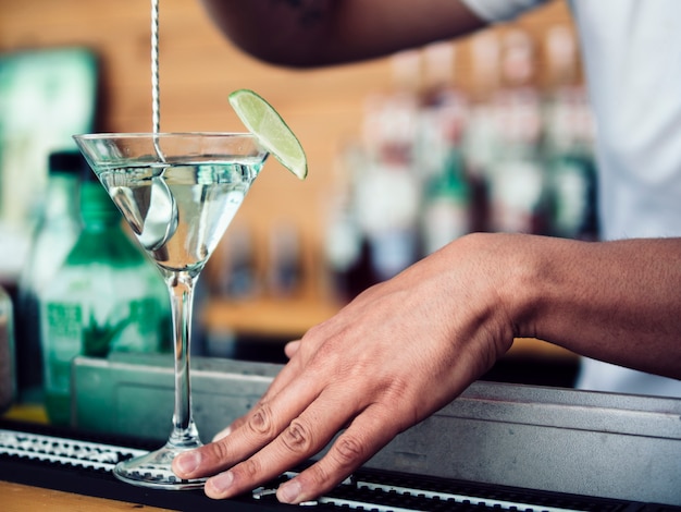 Barista maschio che mescola cocktail in vetro del martini