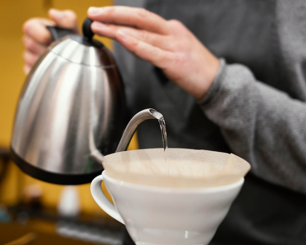 Barista maschio con grembiule che versa acqua nel filtro da caffè