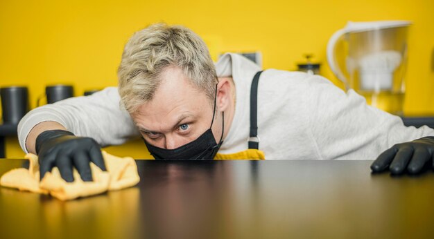 Barista maschio con maschera medica e guanti pulizia tavolo