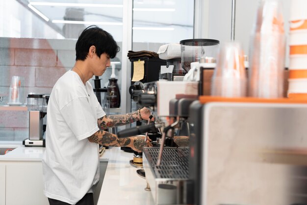 Barista maschio con tatuaggi al lavoro usando la macchina del caffè