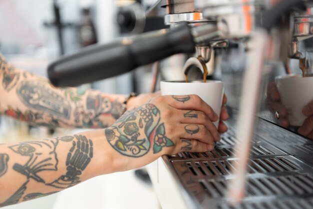 Barista maschio con tatuaggi usando la macchina del caffè al bar