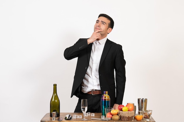 Barista maschio di vista frontale in piedi davanti al tavolo con bevande in posa e pensando sul muro bianco bar notte maschio bere alcolici club