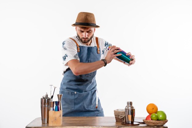 Barista maschio vista frontale davanti al bancone del bar che prepara un drink nello shaker sul muro bianco bar alcol lavoro notturno club di bevande alla frutta