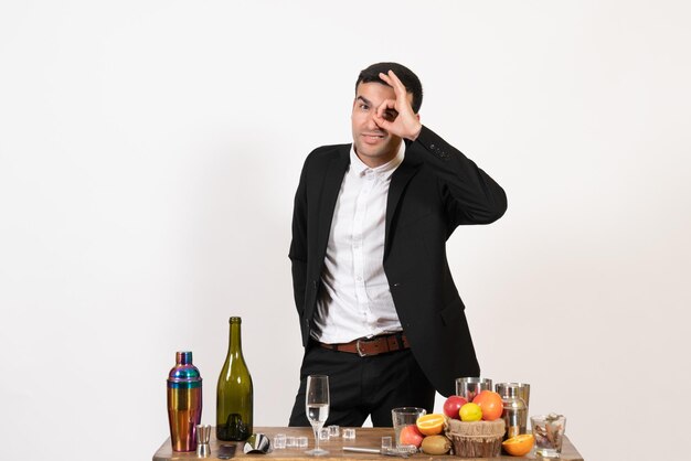 Barista maschio vista frontale in abito classico in piedi davanti al tavolo con bevande sul muro bianco club alcol maschio night bar drink
