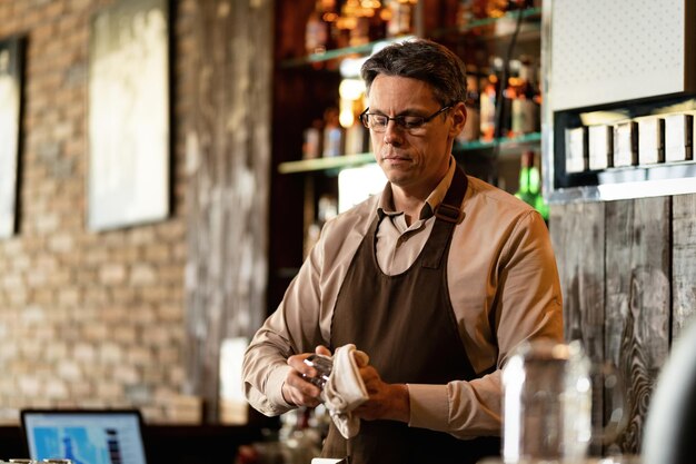 Barista metà adulto che pulisce il bicchiere dopo l'orario di lavoro in un pub