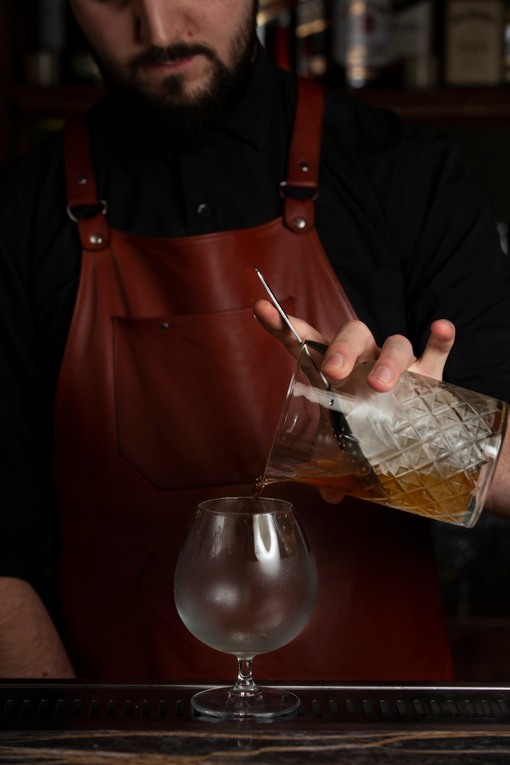 Foto gratuito barista versando drink dal bicchiere di cristallo nel bicchiere da brandy