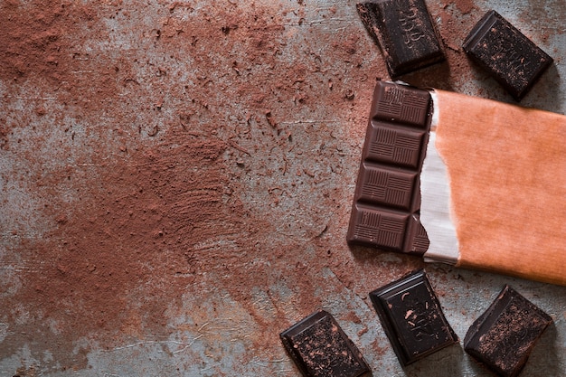 Barretta di cioccolato e pezzi con polvere di cacao su fondo rustico