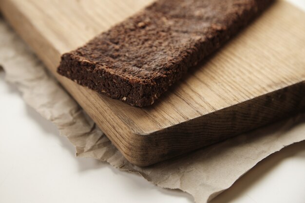 Barretta di cioccolato sano appena sfornato biologico artigianale con frutti di bosco e noci macinate su tavola di legno e carta del mestiere, isolato sul tavolo bianco