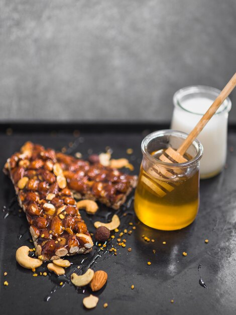 Barrette di muesli di frutta secca con vasi di latte e miele su sfondo nero strutturato