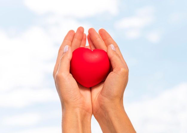 Basso angolo di mani che tengono a forma di cuore con il cielo