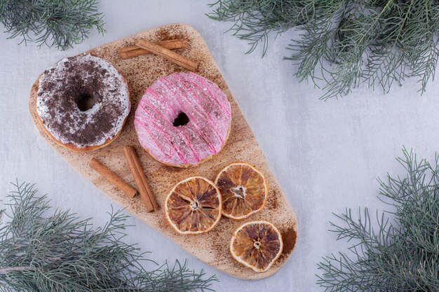 Bastoncini di cannella, ciambelle e fette d'arancia essiccate su una tavola su sfondo bianco.