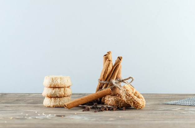 Bastoncini di cannella con biscotti, chiodi di garofano, tovaglietta sul muro di legno e bianco, vista laterale.