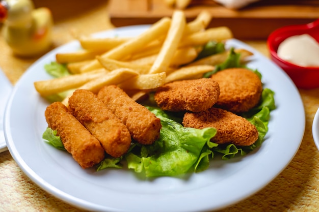 Bastoncini di pollo vista laterale con pepite e patatine fritte su foglia di lattuga