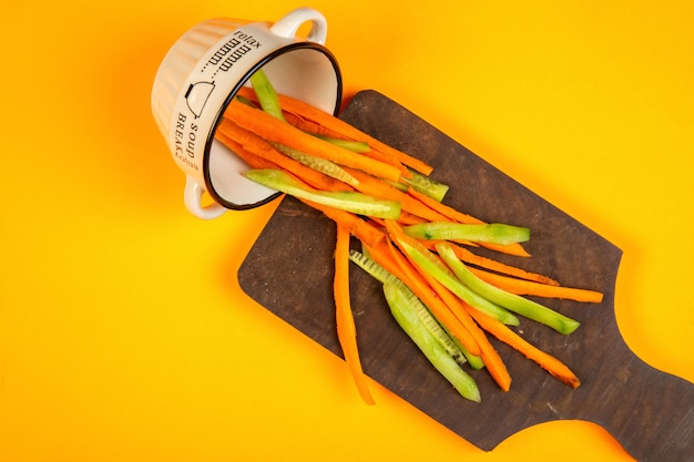 bastoni di carota e cetriolo superiore sul tagliere di legno su giallo